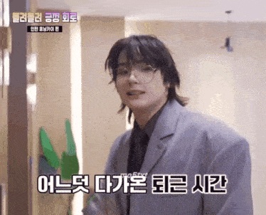 a young man wearing glasses and a suit is standing in a room with chinese writing on the wall