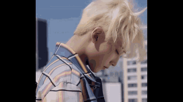 a young man with blonde hair is wearing a plaid shirt and standing in front of a city skyline .