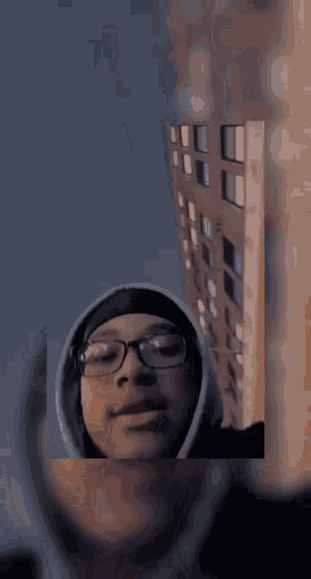 a man wearing glasses and a hooded sweatshirt is standing in front of a building