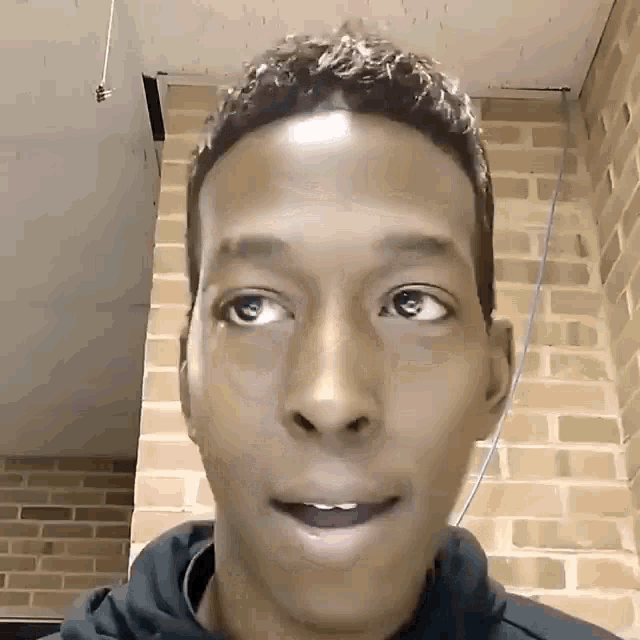 a close up of a person 's face with a brick wall behind him