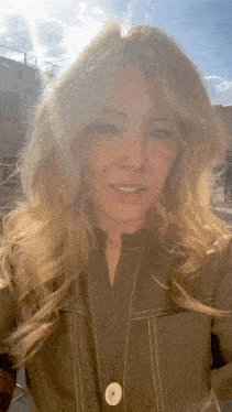 a woman with long blonde hair is standing in front of a building and smiling .