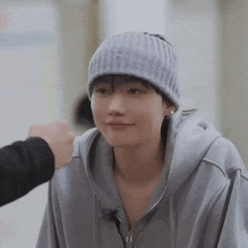 a young man wearing a beanie and a hoodie is being patted by a person .