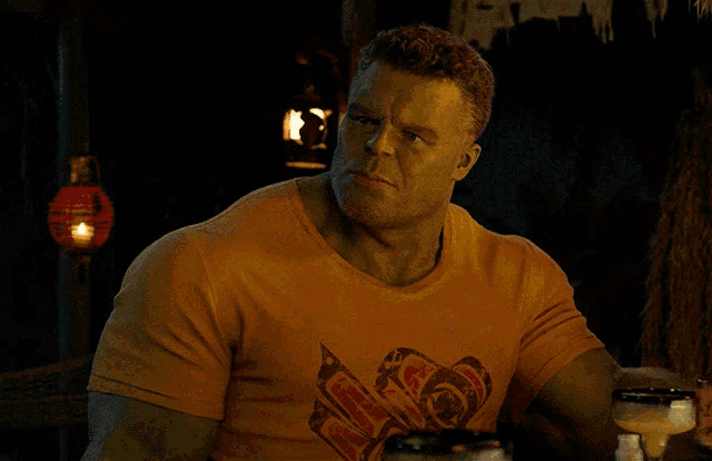 a man with green skin is wearing an orange t-shirt with a heart on it