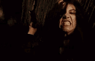 a woman is making a funny face in a dark room while another woman holds her hair .