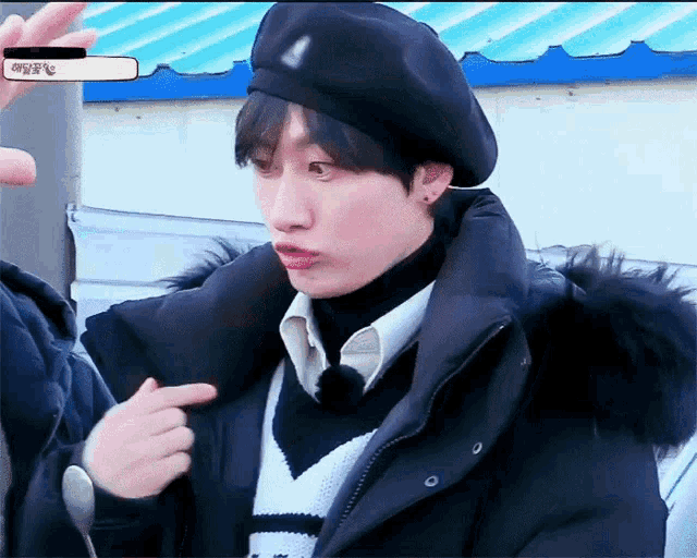 a young man wearing a black beret and a black jacket holds a spoon