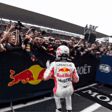 a race car driver wearing a red bull uniform is being congratulated by a crowd