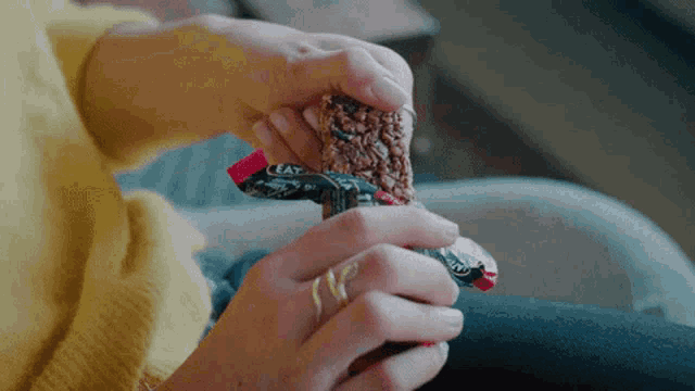 a woman in a yellow sweater is eating a candy bar with the word eat on it