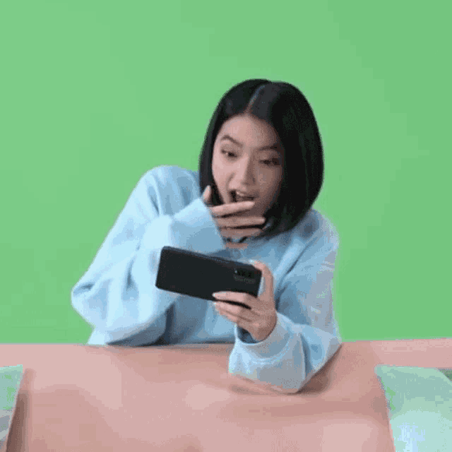 a woman in a blue sweater is sitting at a table looking at her cell phone .