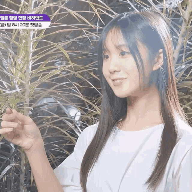 a woman in a white shirt is holding a plant in front of a sign that says ' korean ' on it