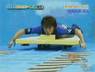 a man in a blue shirt is laying on a yellow board in a pool