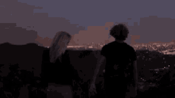 a woman is standing on top of a hill looking at the city lights .