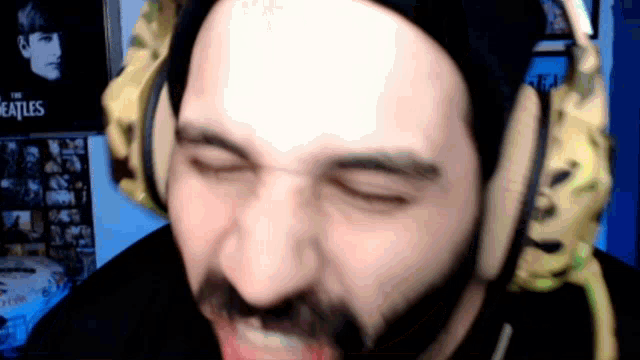 a man with a beard wearing headphones and a beatles poster on the wall behind him