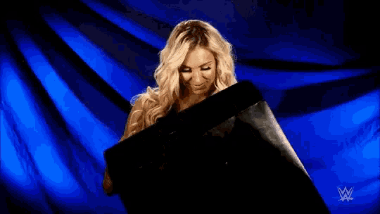 a woman is holding a black box and smiling in front of a blue curtain .