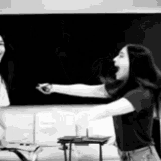 a black and white photo of two women standing in front of a chalkboard .
