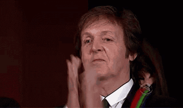 a man wearing a suit and tie is clapping his hands