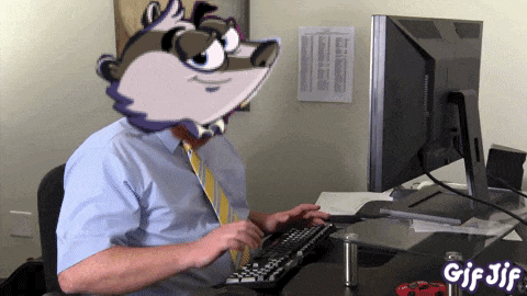 a man sitting at a desk with a cartoon raccoon on his head