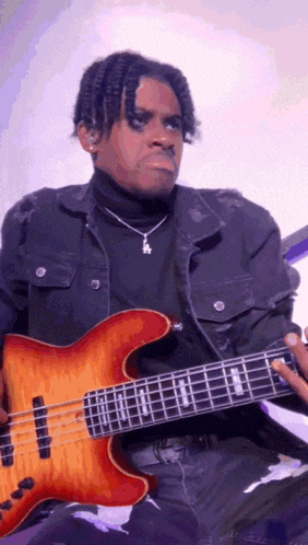 a man playing a bass guitar with a necklace that has the letter a on it