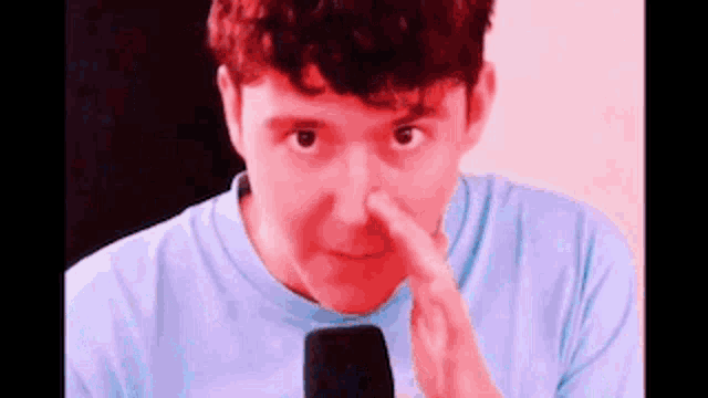 a man is holding his nose while wearing a blue shirt .