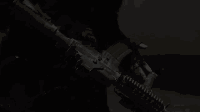 a person is holding a rifle in their hand in the dark .