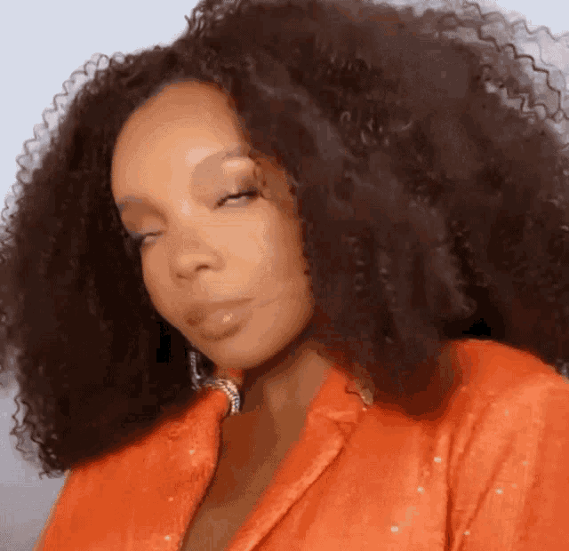 a woman with curly hair is wearing an orange jacket