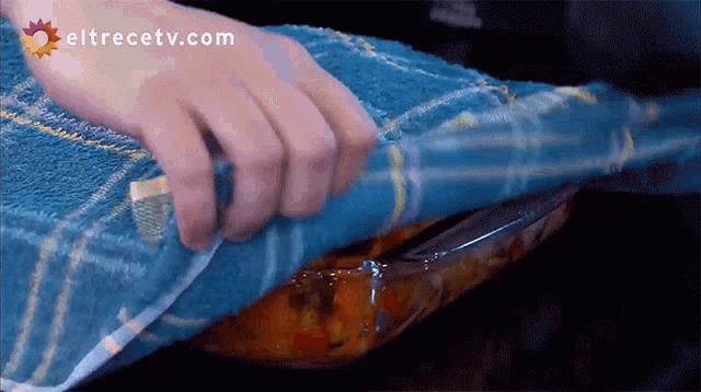 a person covering a casserole dish with a blue towel with eltrecetv.com written on the bottom right