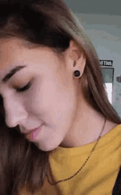 a close up of a woman 's face with a yellow shirt and black earrings .