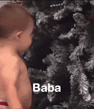 a baby is standing in front of a christmas tree with the word baba written on it .