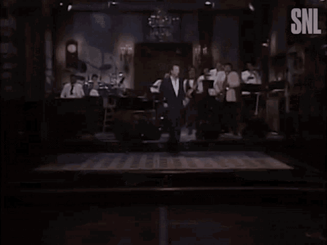 a man in a suit dancing in front of a snl banner