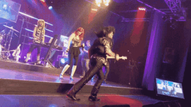 a man playing a guitar on a stage with a woman standing behind him