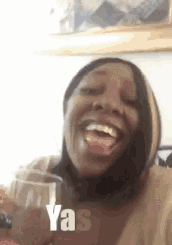 a woman is holding a glass of wine and making a funny face with the word yas in the corner .