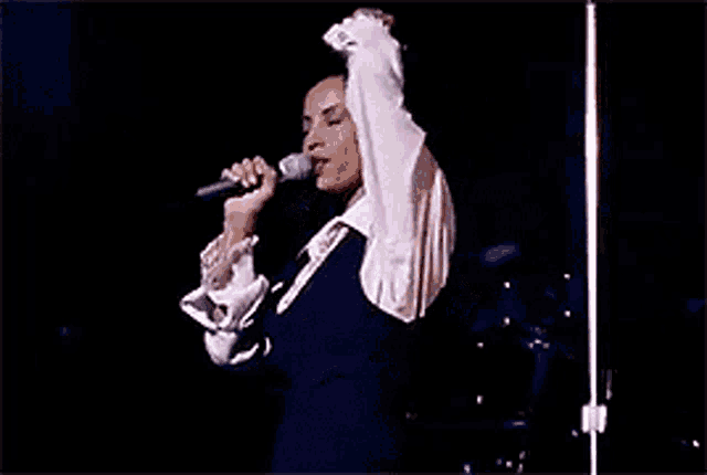 a woman in a pink shirt is singing into a microphone