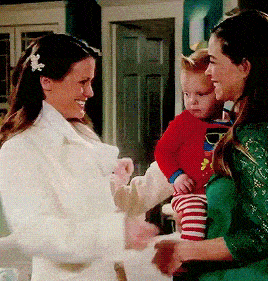 a woman in a white coat holds a baby in a superman sweater