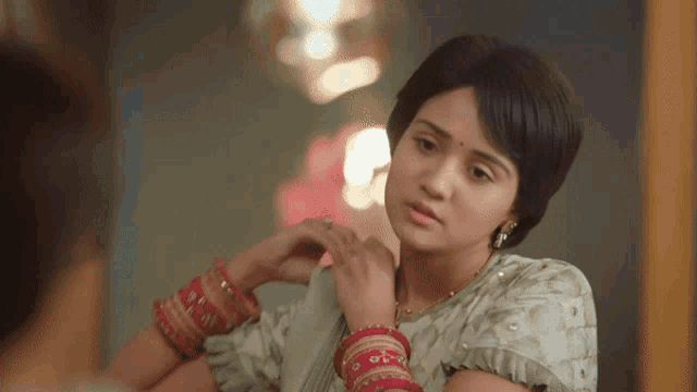 a woman is looking at herself in a mirror while wearing bangles
