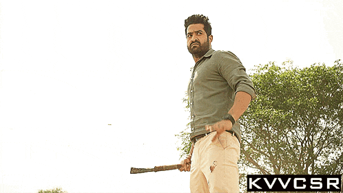 a man holding a stick in front of trees with a kvvcsr logo in the corner