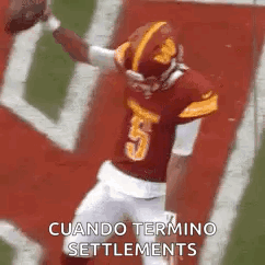 a football player in a red jersey is jumping in the air while holding a ball .