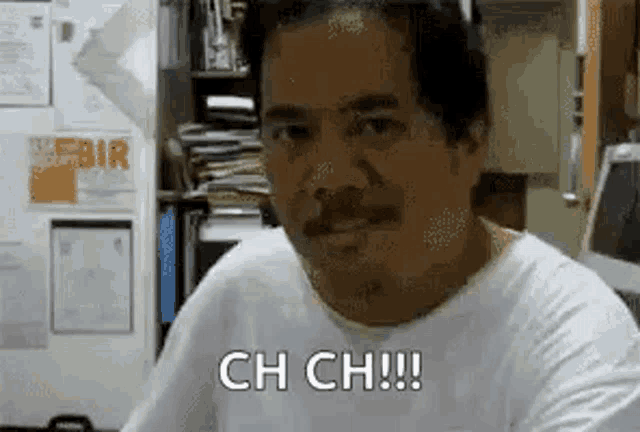 a man with a mustache is sitting at a desk in an office and making a funny face .