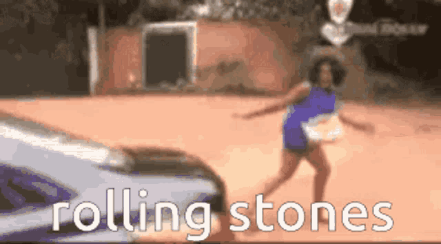 a woman is dancing in front of a car and the words rolling stones are visible