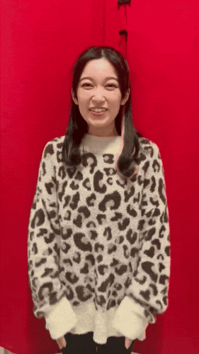 a woman wearing a leopard print sweater smiles in front of a red wall