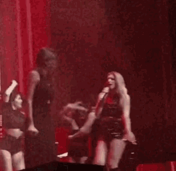 two women are singing into microphones on a stage in front of a red curtain .