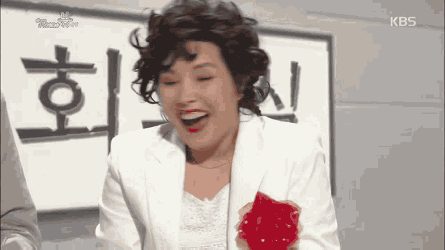 a woman in a white suit is laughing in front of a sign that has kbs written on it