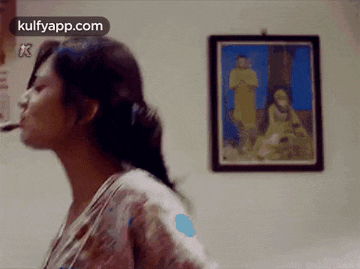 a woman is smoking a cigarette in front of a painting on the wall .