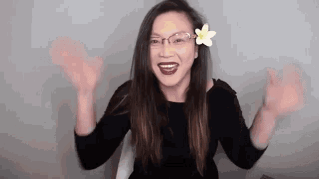 a woman wearing glasses and a flower in her hair is waving her hands in the air .
