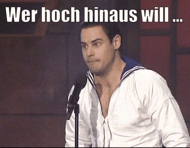 a man in a white jacket stands in front of a microphone with the words wer hoch hinaus will above him
