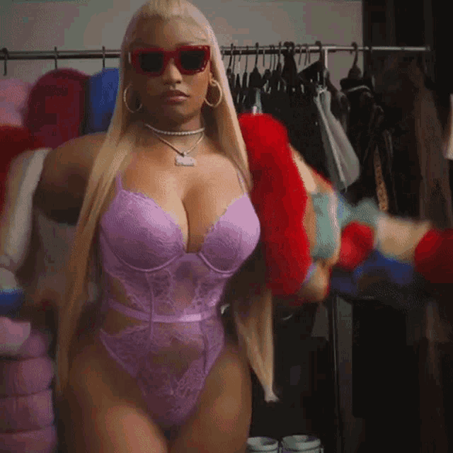 a woman wearing sunglasses and a purple bodysuit is standing in front of a clothes rack .