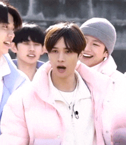 a group of young men are standing together and one of them is wearing a pink jacket and a beanie