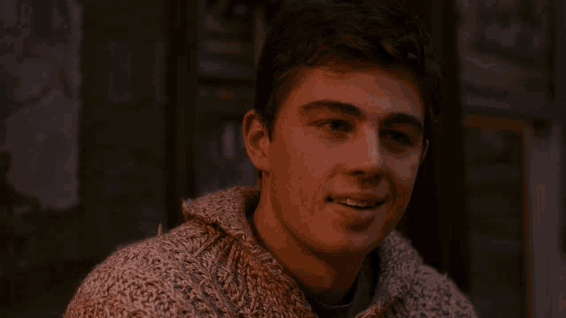 a young man in a sweater is smiling and looking at the camera