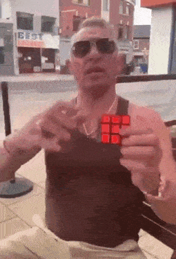 a man is holding a red rubik 's cube in front of a building that says best
