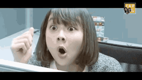 a woman is making a surprised face while sitting at a desk in front of a computer .
