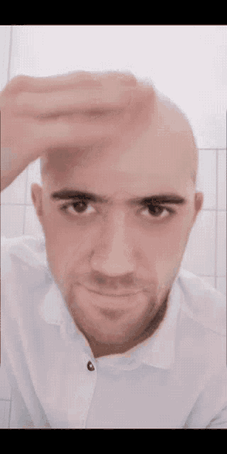 a man with a shaved head looks at the camera with his hand on his forehead