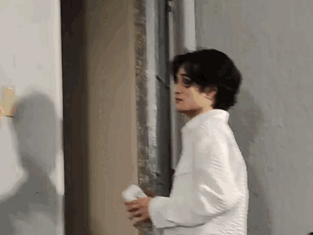 a man in a white shirt is standing next to a wall and holding a napkin .